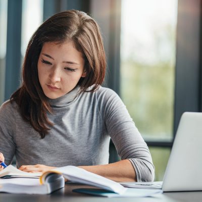 Shot of young woman taking down notes in diary. Female university student preparing note for the exam at library.